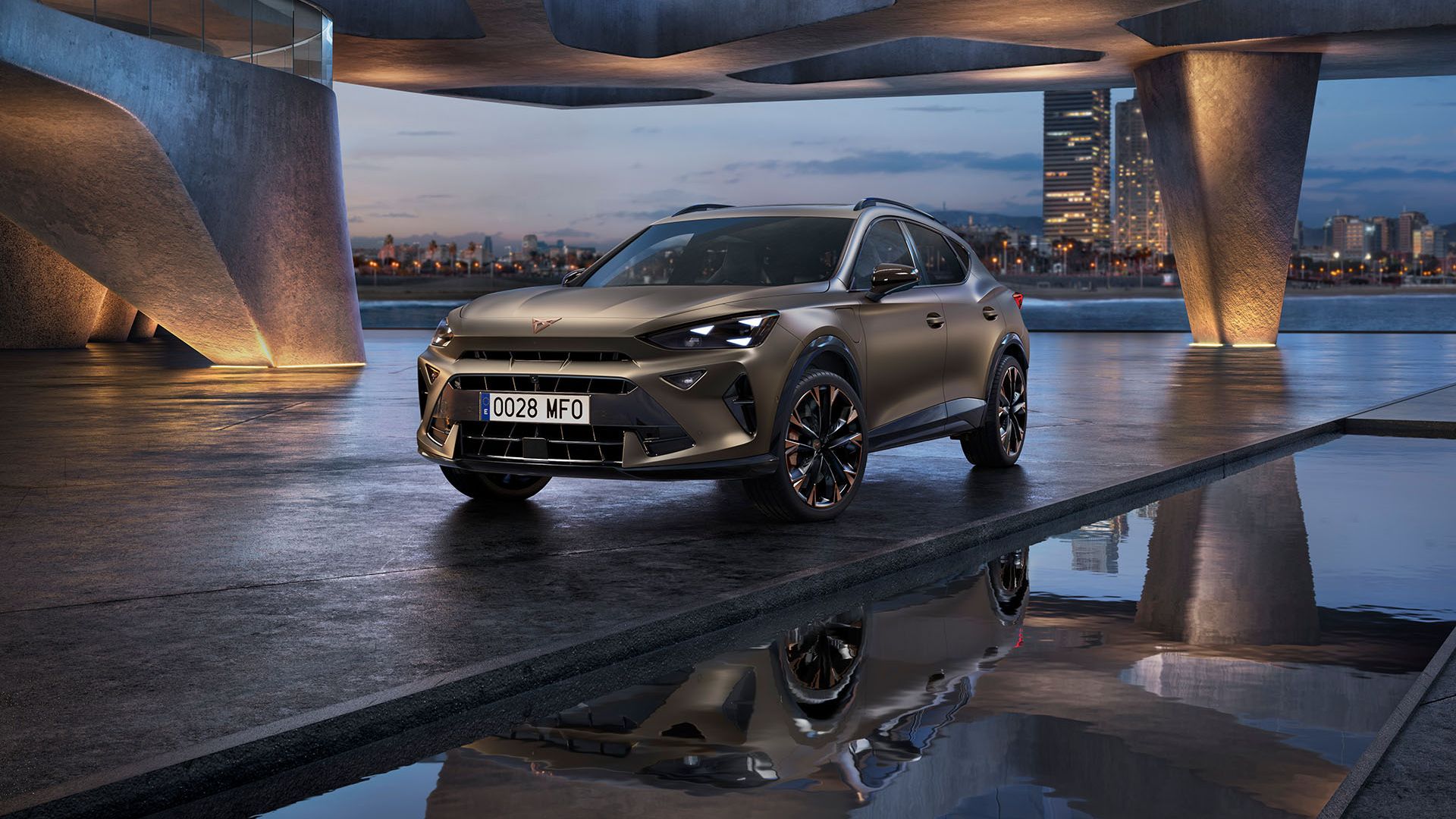 CUPRA Formentor SUV coupé 2025 estacionado sob uma construção curva de betão, perto de uma superfície de água refletora, com uma paisagem urbana crepuscular ao fundo, com arranha-céus iluminados.