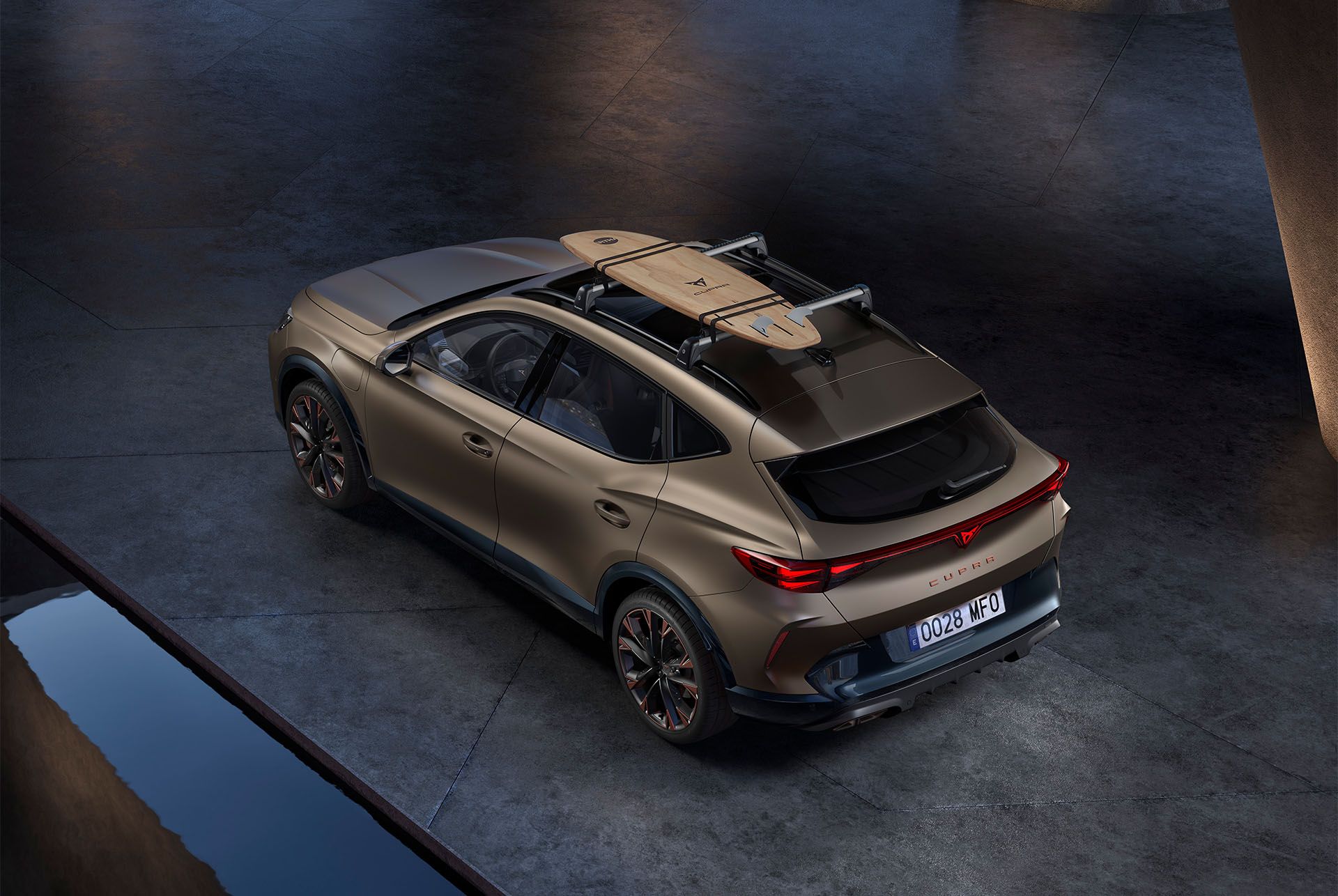 Vista aérea do CUPRA Formentor em century bronze mate, com um acessório de suporte para pranchas de surf no tejadilho do carro, estacionado.
