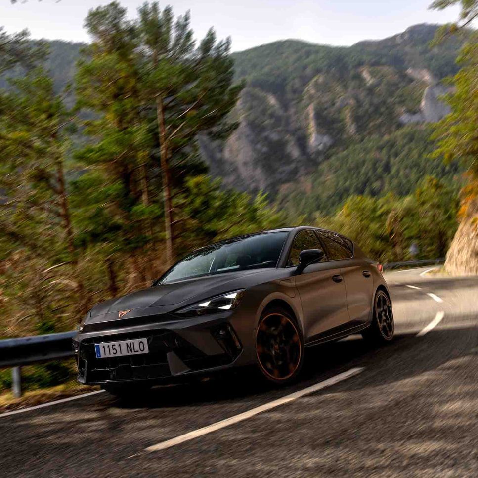 Vista lateral traseira do novo automóvel desportivo e aerodinâmico CUPRA Leon Sportstourer 2025 em cinzento mate, estacionado num passeio durante o anoitecer. 
