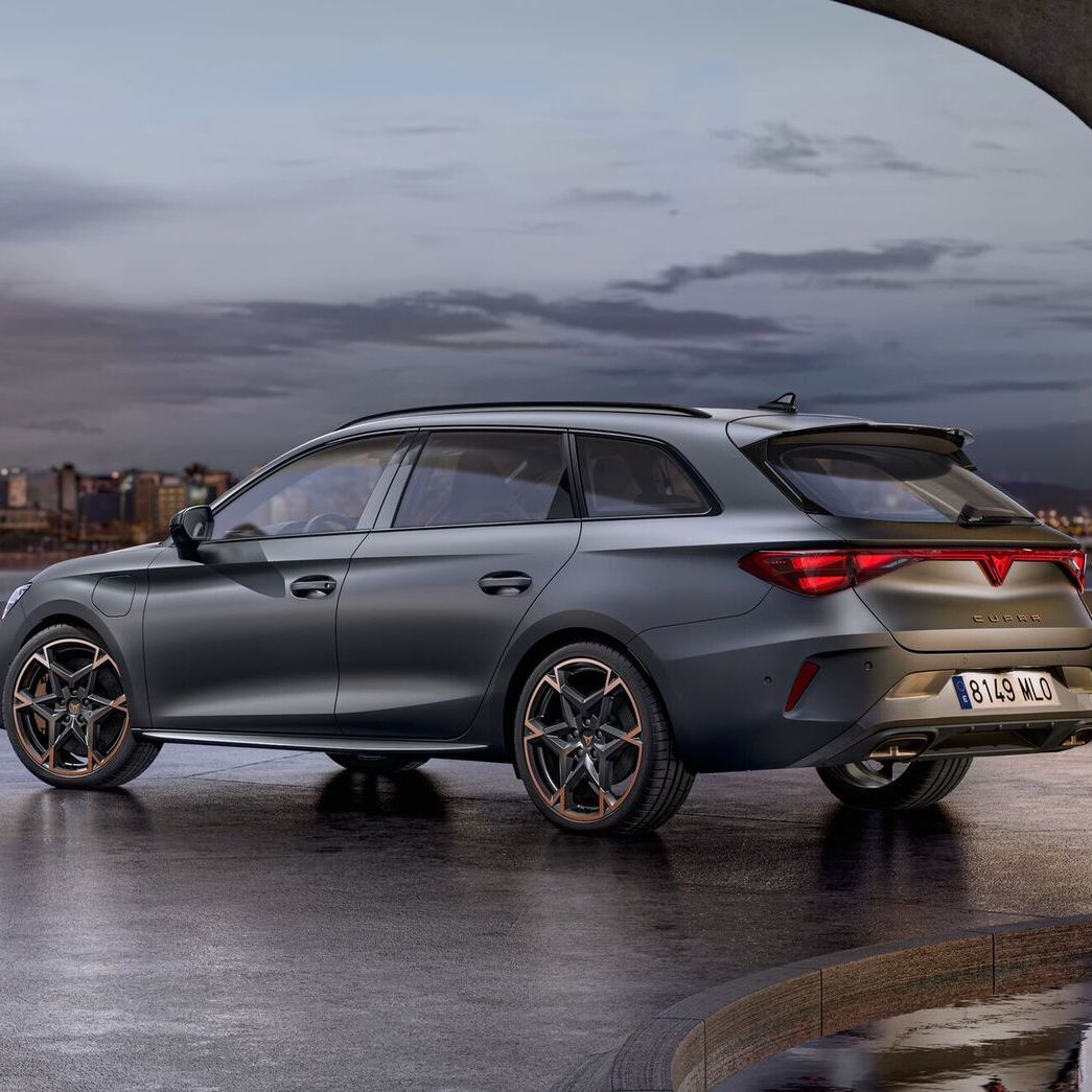 Vista lateral traseira do novo automóvel desportivo e aerodinâmico CUPRA Leon Sportstourer 2025 em cinzento mate, estacionado num passeio durante o anoitecer. 