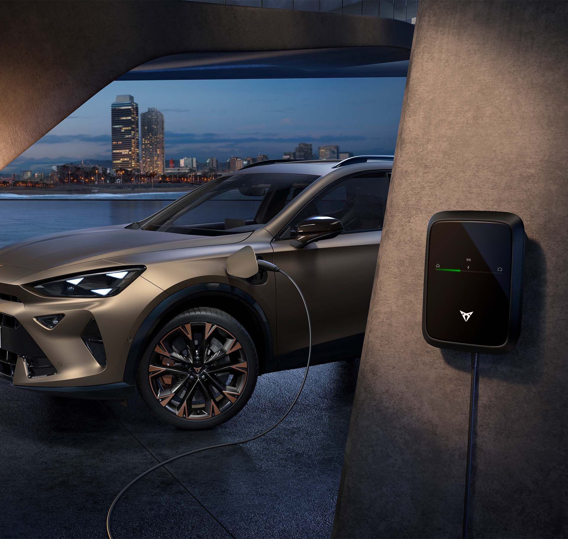 Vista frontal esquerda do CUPRA Formentor 2024 em century bronze mate com jantes em cobre, a carregar, com vista de fundo da paisagem urbana de Barcelona ao entardecer