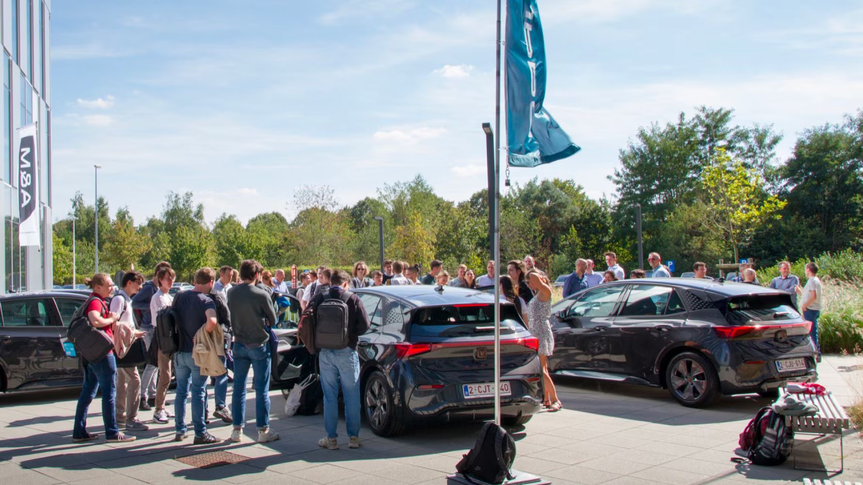Veículos elétricos de empresa CUPRA Born estacionados junto aos escritórios da Cegeka, com árvores e céu azul.