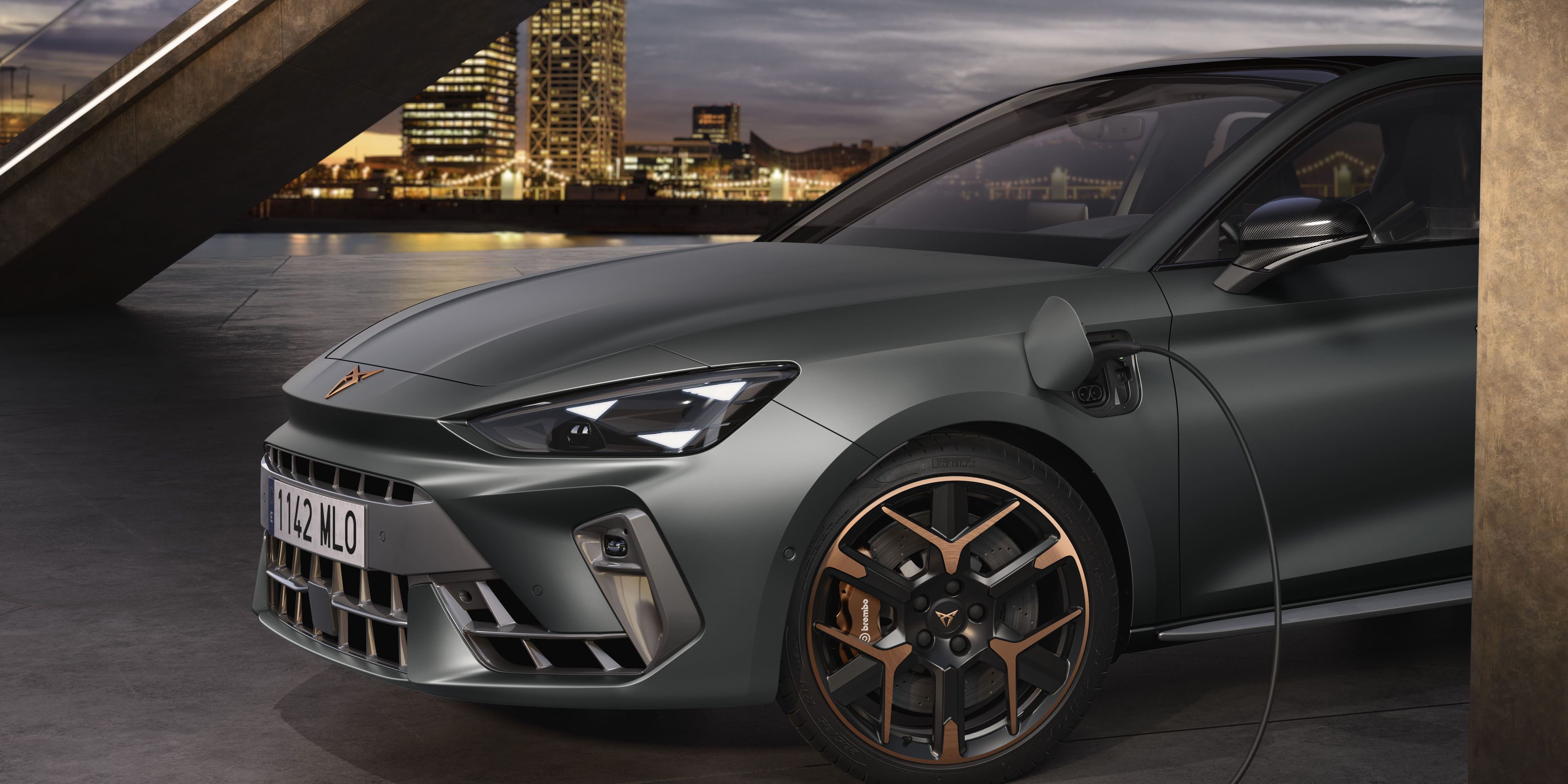 Vista lateral dianteira do novo cupra leon sportstourer 2025 em cinzento enceladus, ligado à corrente e a carregar. Design angular dos faróis e jantes de liga leve com detalhes em cobre.