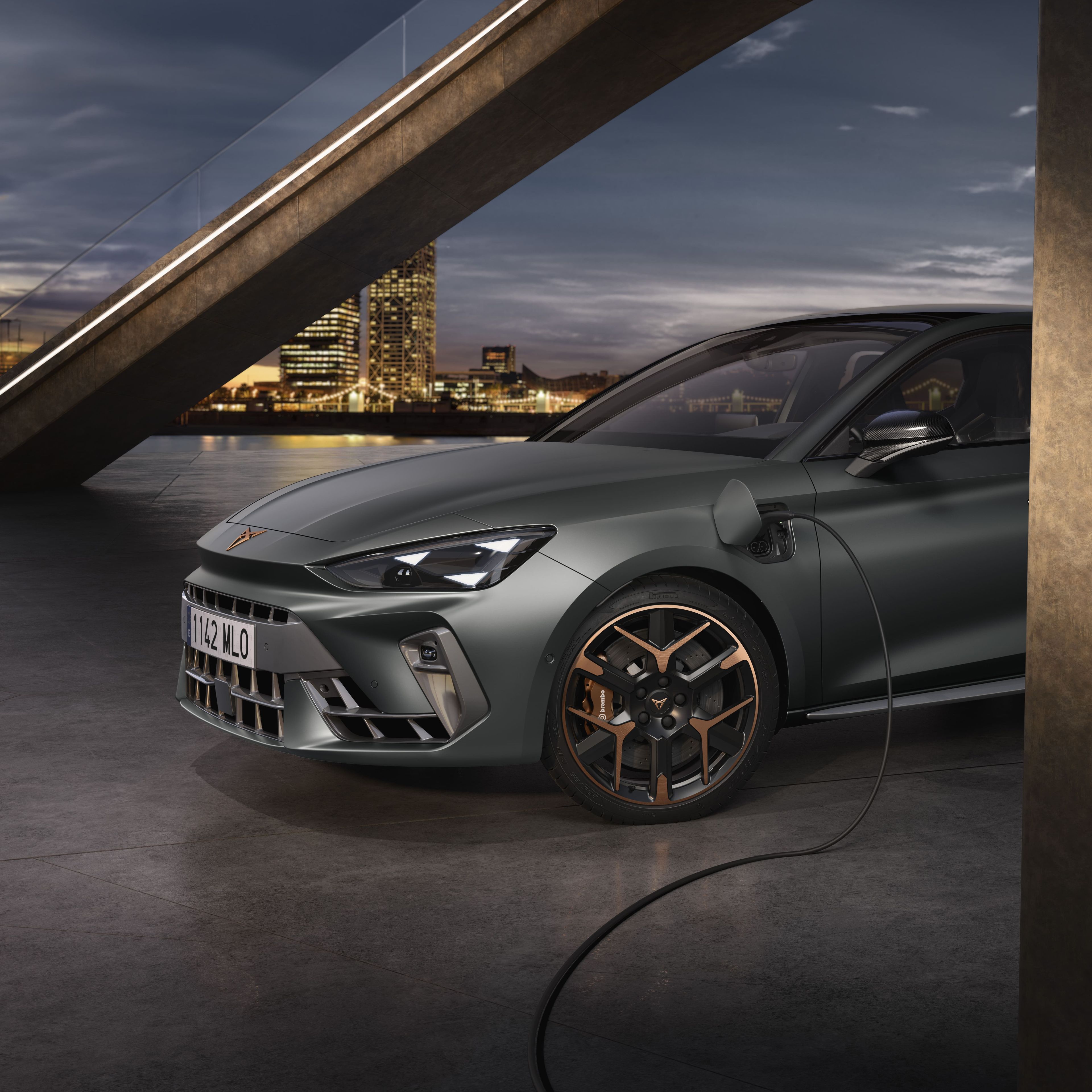 Vista lateral dianteira do novo cupra leon sportstourer 2025 em cinzento enceladus, ligado à corrente e a carregar. Design angular dos faróis e jantes de liga leve com detalhes em cobre.