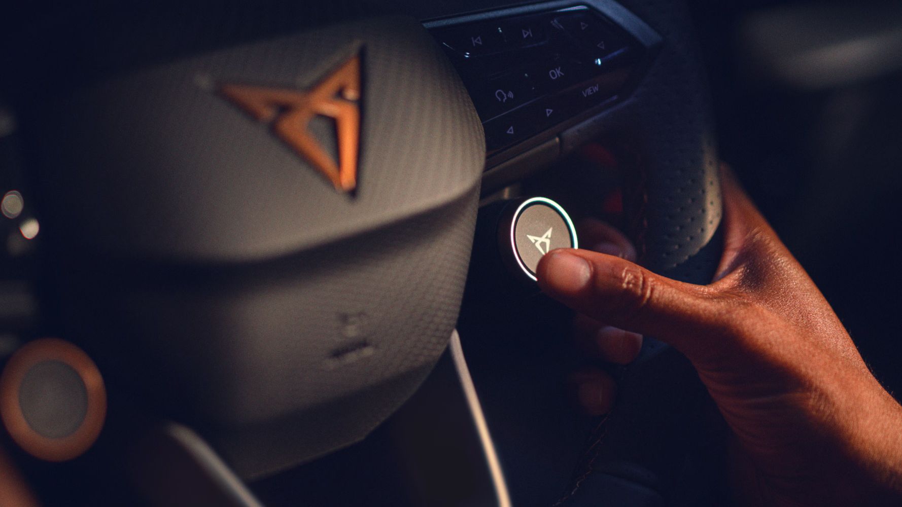 Volante do CUPRA Born com botões satélite e logótipo CUPRA em cobre, close-up no interior de viatura de empresa.