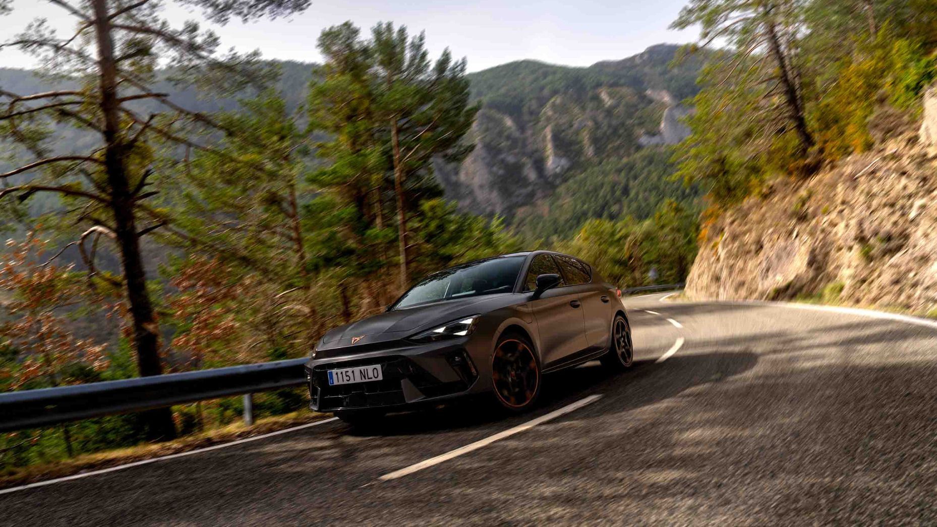 Vista lateral traseira do novo automóvel desportivo e aerodinâmico CUPRA Leon Sportstourer 2025 em cinzento mate, estacionado num passeio durante o anoitecer. 