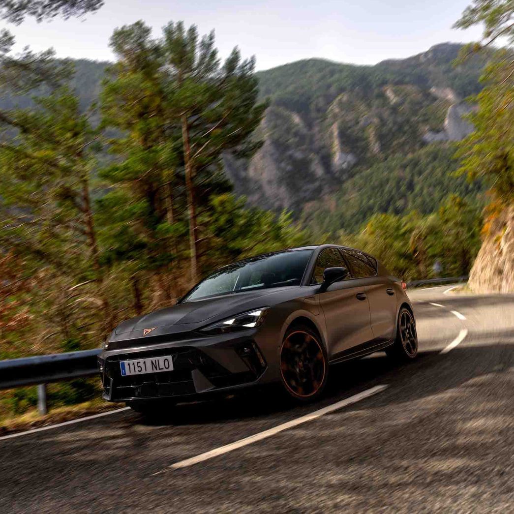 Vista lateral traseira do novo automóvel desportivo e aerodinâmico CUPRA Leon Sportstourer 2025 em cinzento mate, estacionado num passeio durante o anoitecer. 