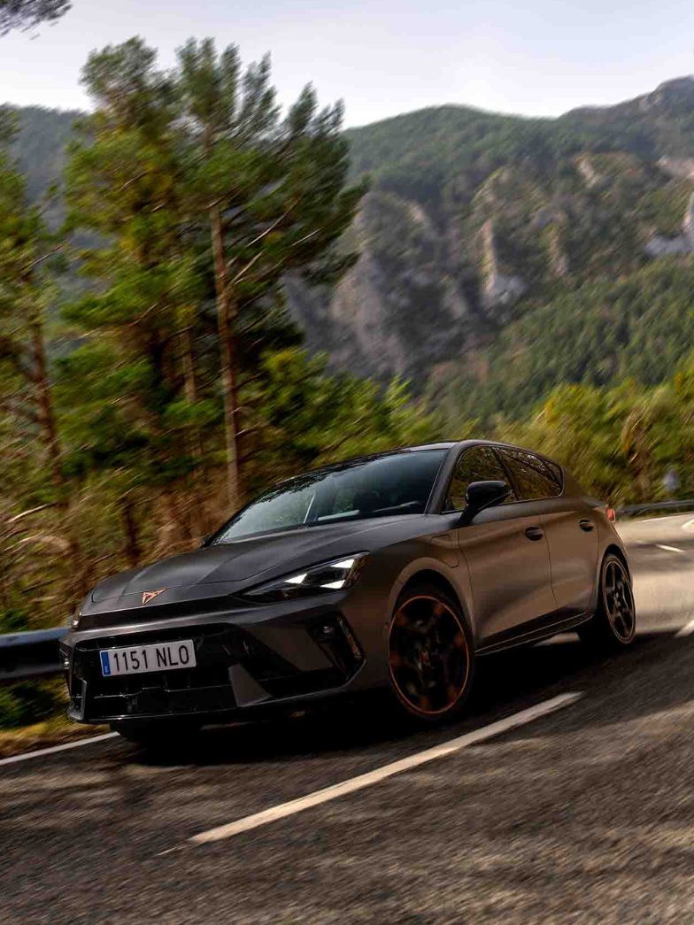 Vista lateral traseira do novo automóvel desportivo e aerodinâmico CUPRA Leon Sportstourer 2025 em cinzento mate, estacionado num passeio durante o anoitecer. 
